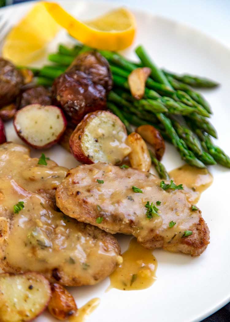 Lemon, Rosemary Pork Medallions served on white plate with potatoes and asparagus.
