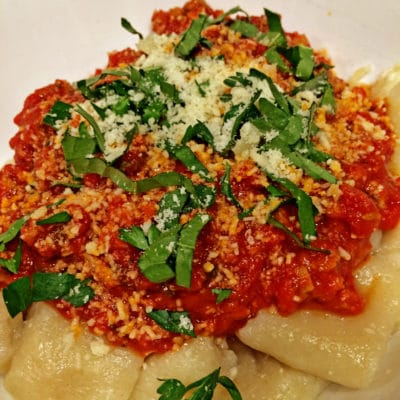 A plate of food with tomato sauce, herbs, with Gnocchi