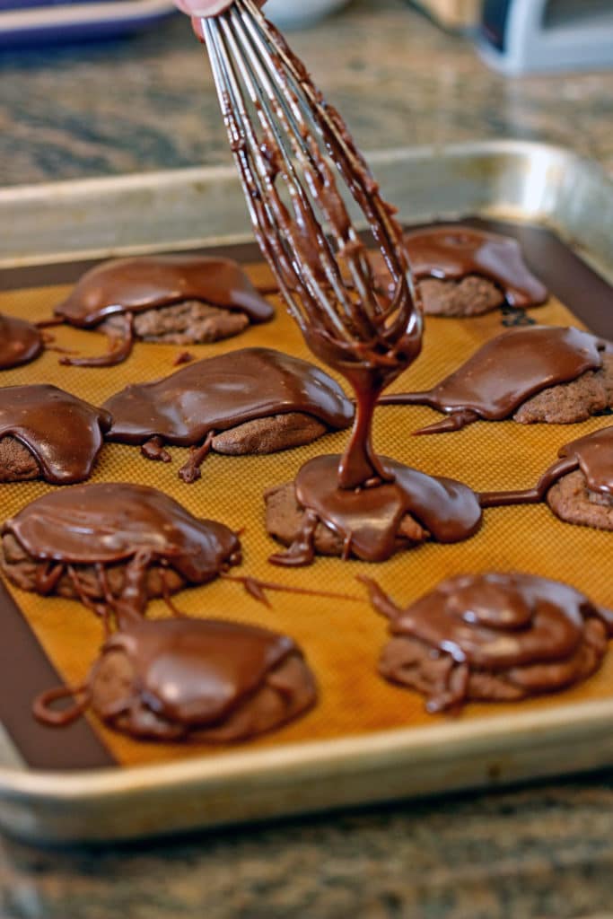 drizzling chocolate ganache with whisk onto homemade chocolate cookies