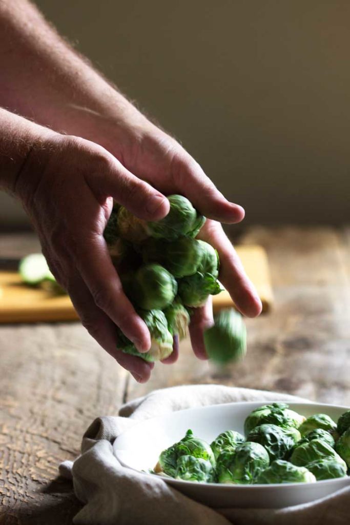 man's hands tossing fresh brussels sprouts into white bowl