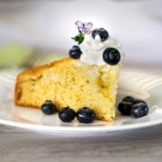 A close up of a piece of lemon rosemary cake on a plate with blueberries