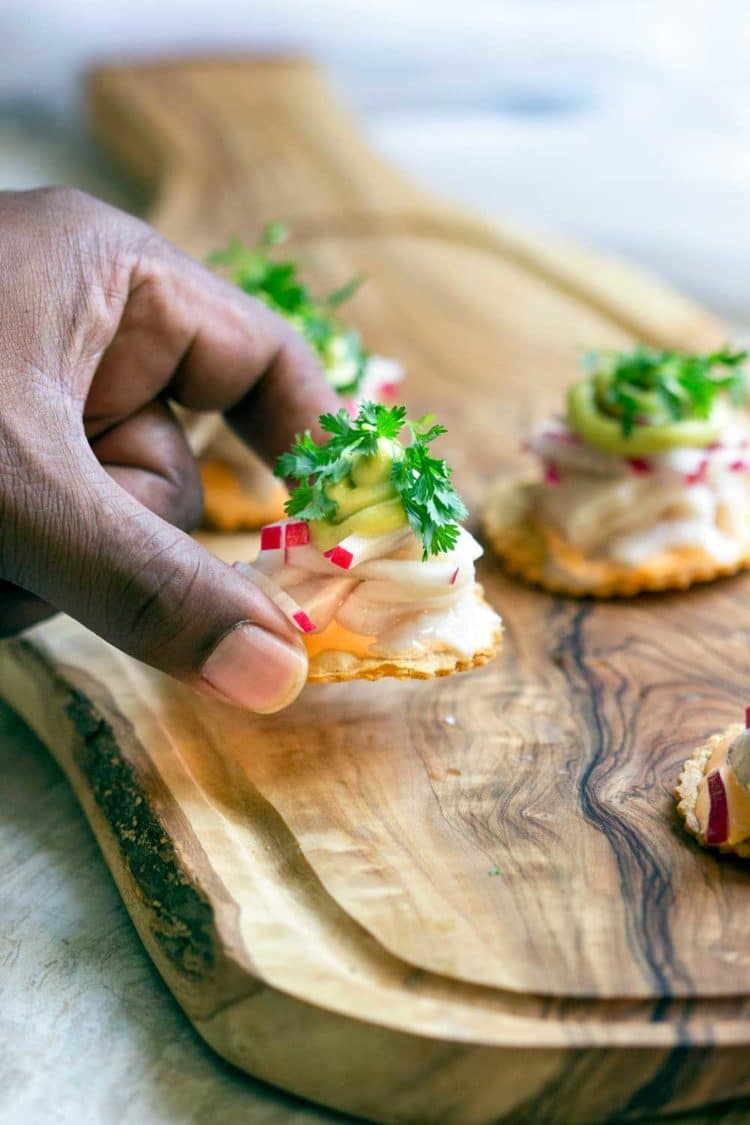 closeup: hand lifting up a ceviche tostada off of a wooden cutting board