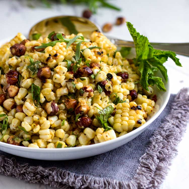 grilled corn salad with hazelnuts with fresh herbs in a white bowl with a large spoon