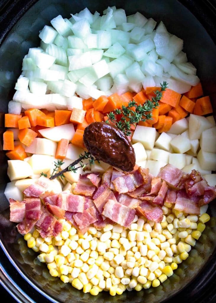 overhead: diced potatoes onions and carrots with bacon and corn in crock pot