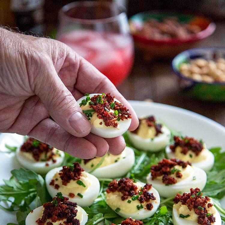 spicy deviled eggs on platter, man's hand holding one