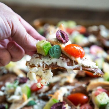 These Greek Styled Pita Chicken Nachos are a great party appetizer or main meal. Loaded with rotisserie chicken, a deconstructed Greek salad and lots of cheese! keviniscooking.com