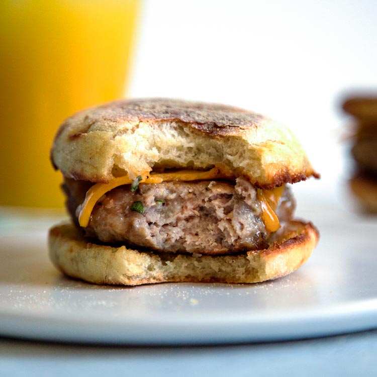side view: english muffin breakfast sandwich with homemade breakfast sausage with a bite taken out