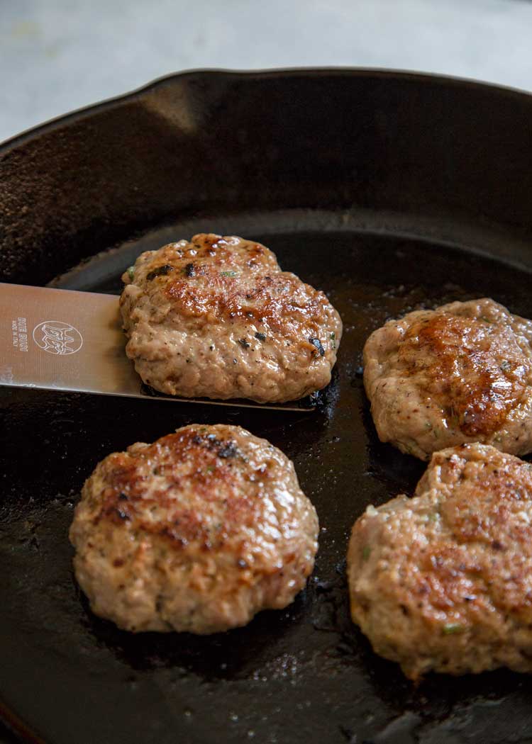 closeup: cooking breakfast sausage recipe in a skillet with a spatula lifting one patty