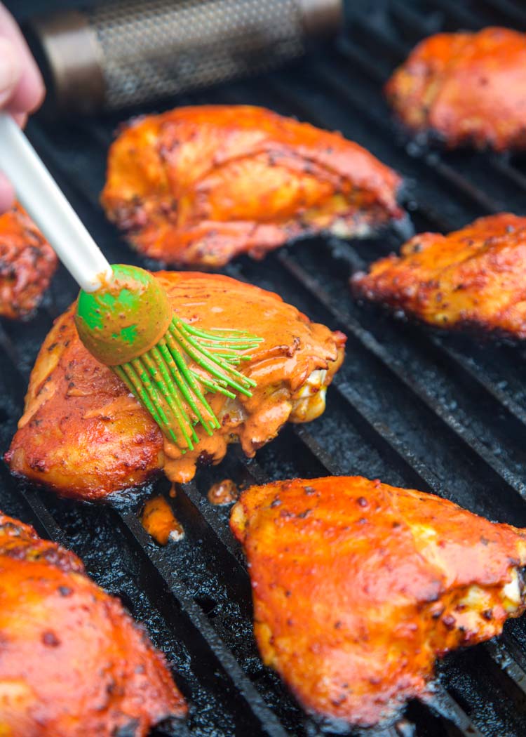 brushing marinade onto pieces of pollo asado on a grill