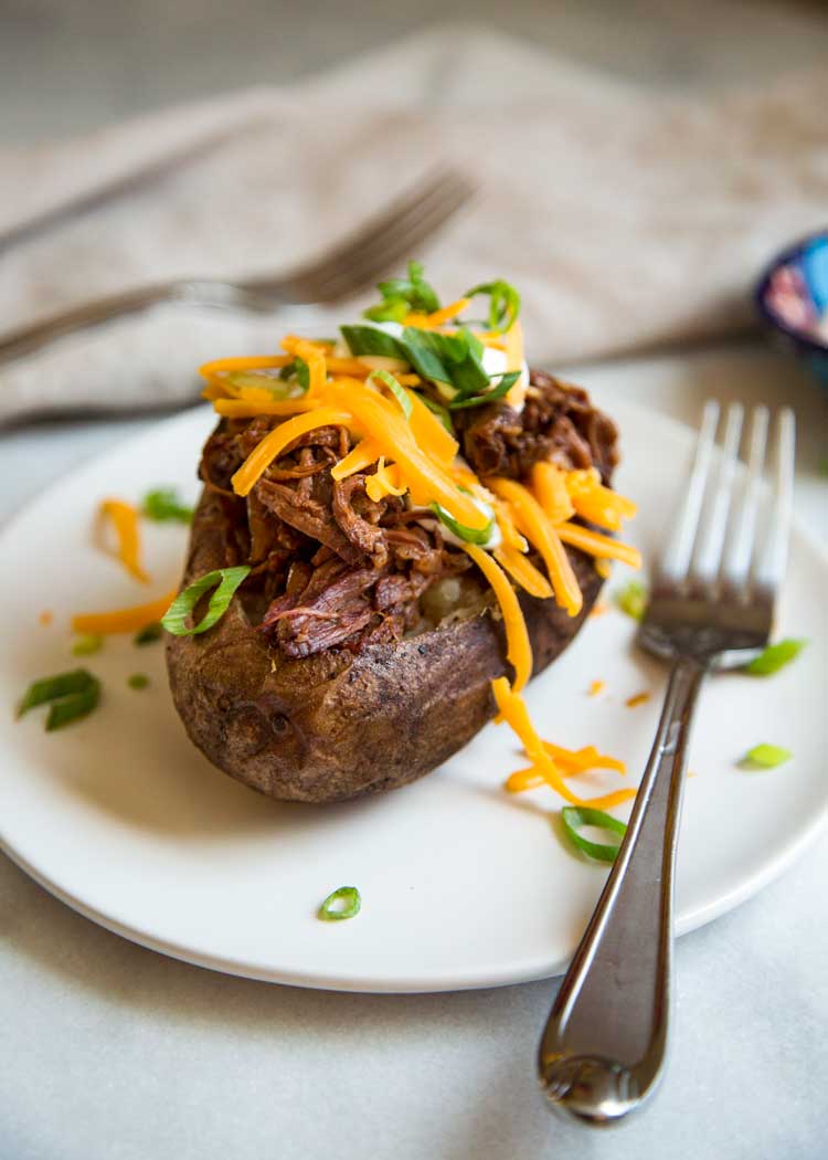 BBQ Beef Stuffed Potatoes on a white plate with cheese and green onions