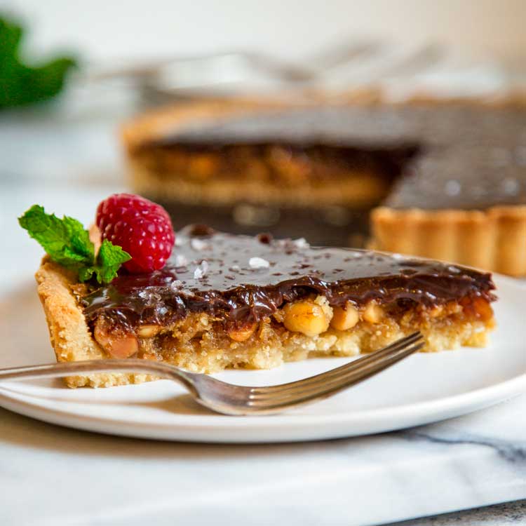 This Chocolate Macadamia Nut Tart has a pastry shell filled with macadamia nuts, caramel studded with chunks of ginger all topped with a chocolate ganache. keviniscooking.com