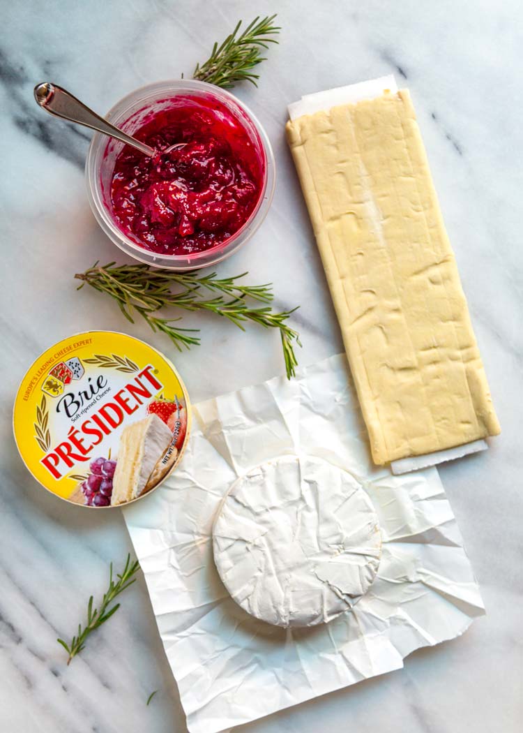 overhead: brie wheel next to red jam and puff pastry for brie puff pastry appetizer recipe