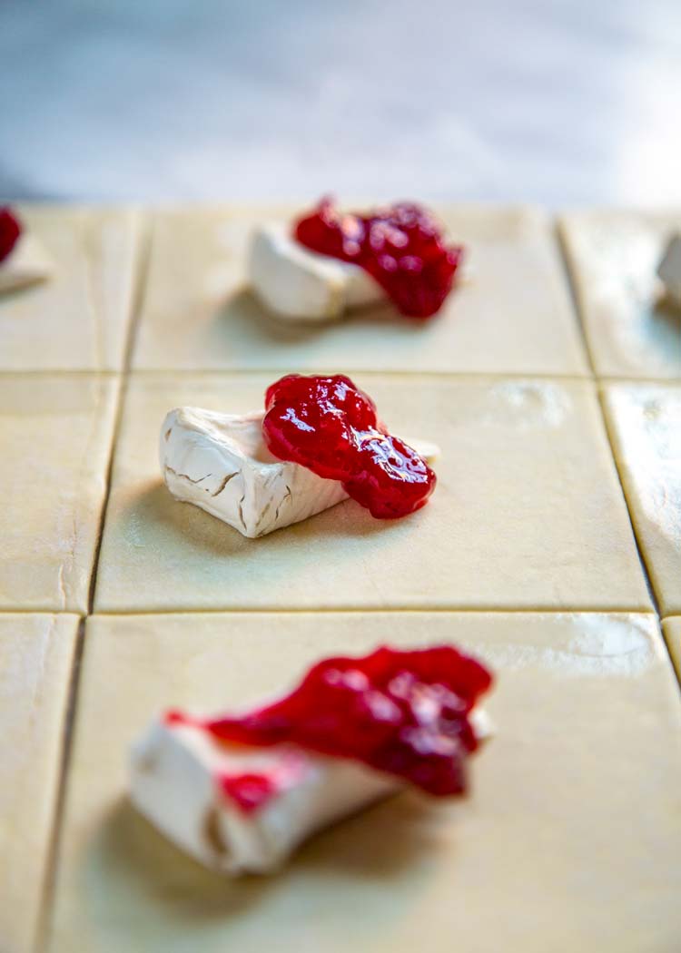 squares of unbaked dough topped with white cheese and pomegranate jam
