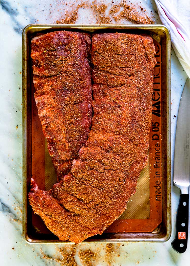 2 racks of baby back ribs rubbed with seasoning on baking sheet