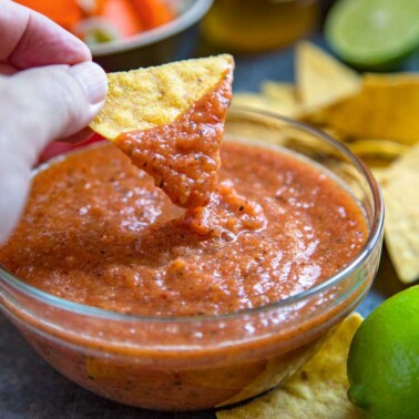 dipping corn tortilla chip into spicy red Mexican condiment