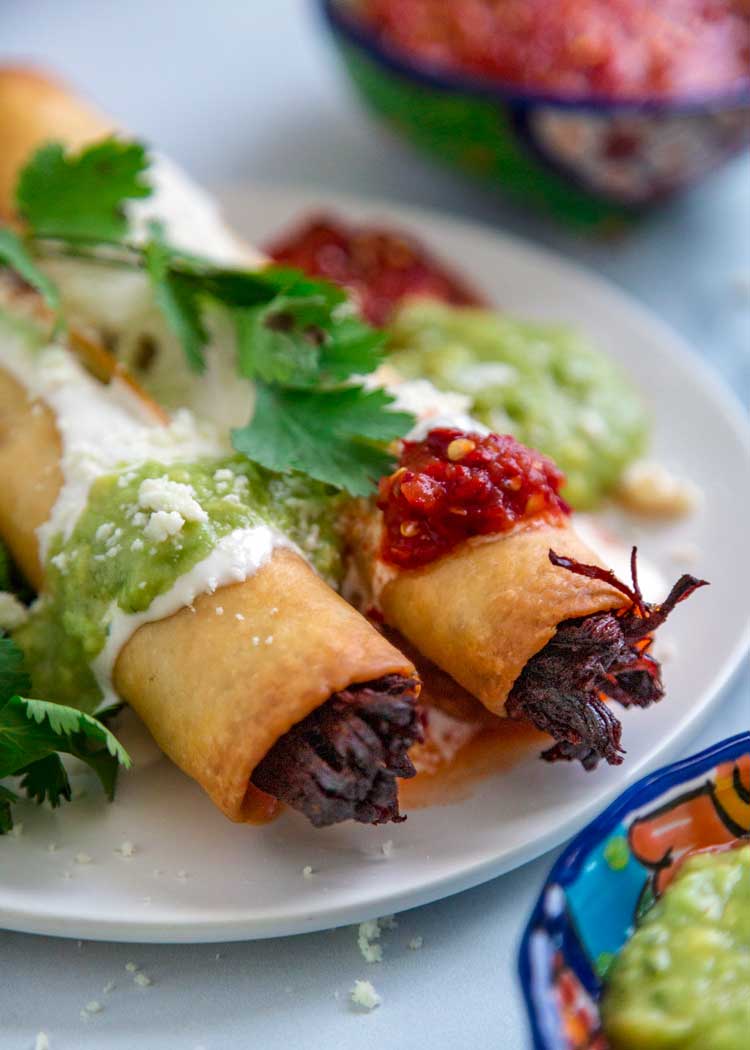 2 Crispy Beef Flautas with guacamole and salsa on a plate