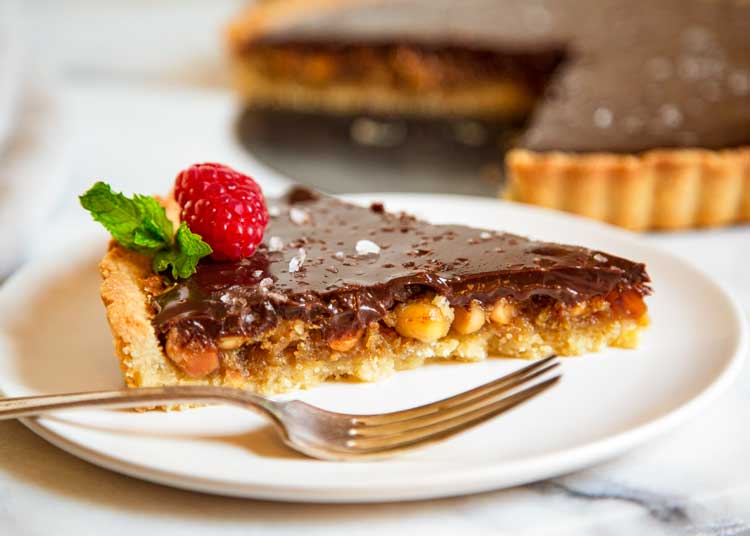 This Chocolate Macadamia Nut Tart has a buttery pastry shell filled with macadamia nuts, a caramel filling studded with chunks of ginger all topped with a chocolate ganache. keviniscooking.com