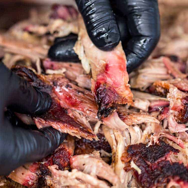 close up of black gloved hands pulling smoked pork butt