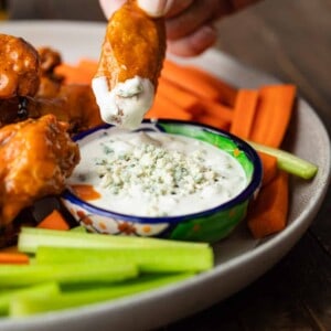 A close up of a plate of crispy baked Chicken wings with buffalo sauce dipping in bleu cheese dressing