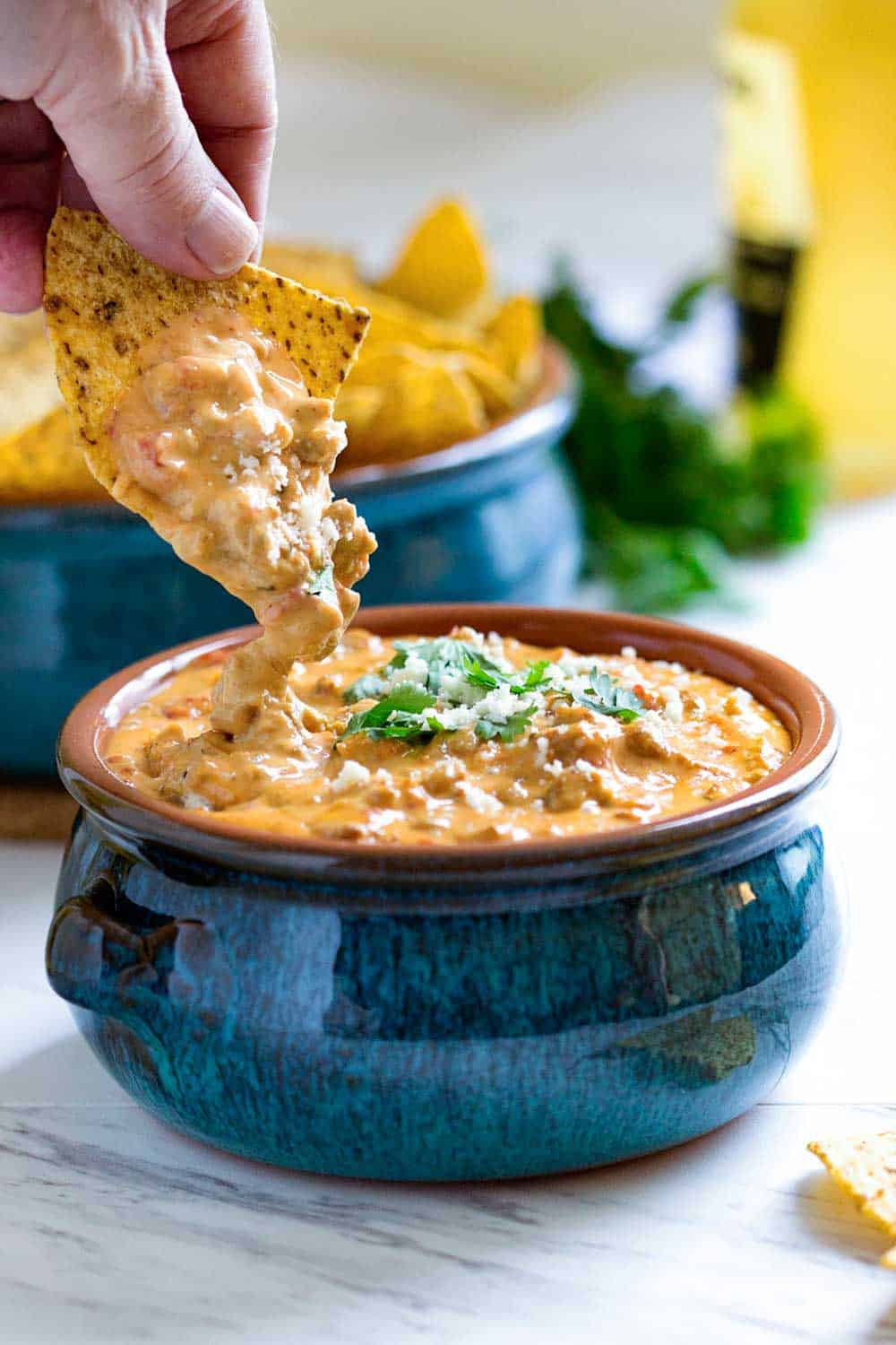 dipping tortilla chips into queso dip made from scratch in a blue crock
