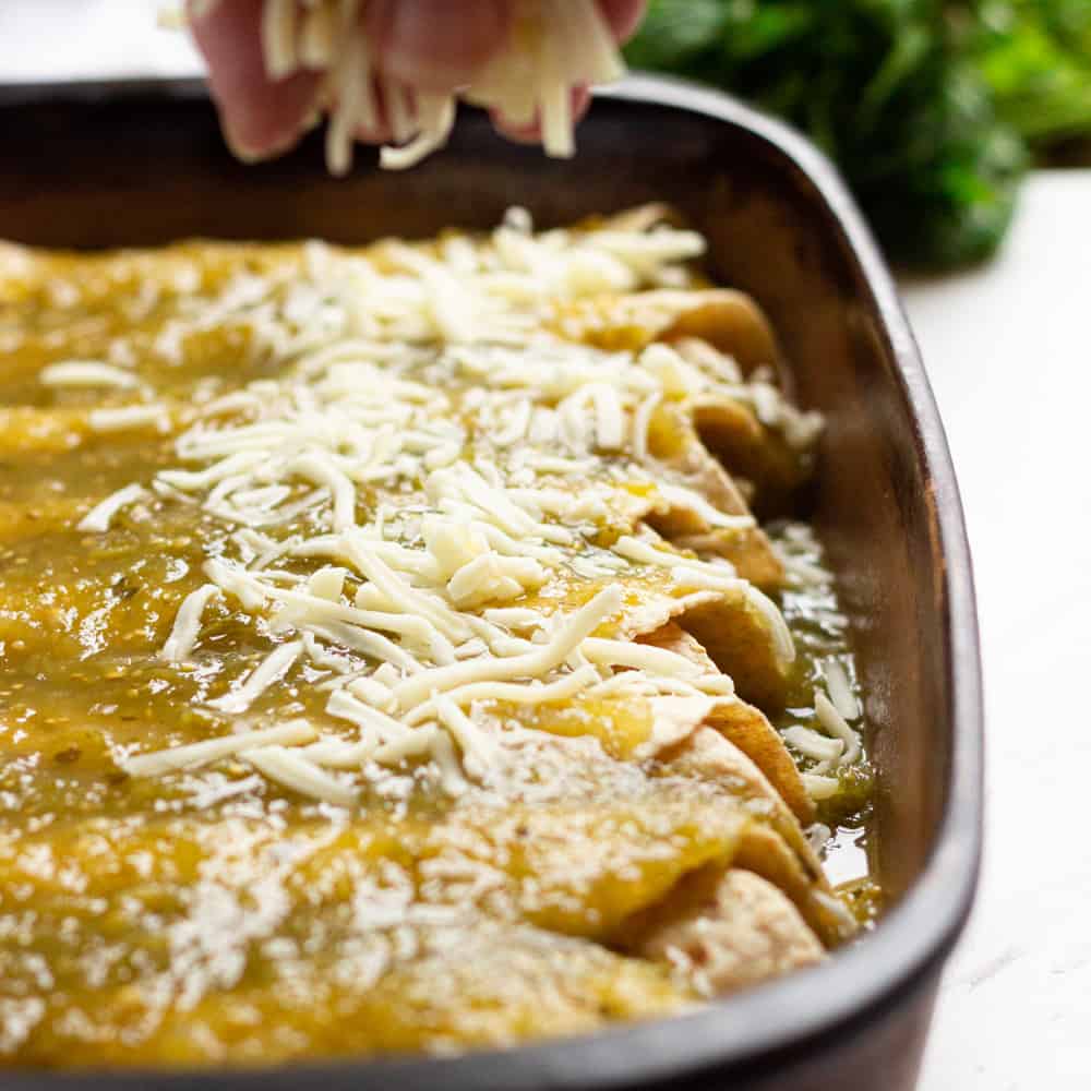 A casserole dish with enchiladas, cheese and green sauce