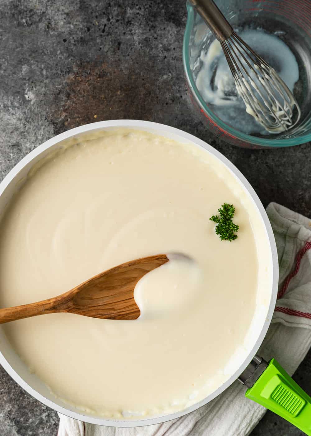 homemade bechamel sauce in white skillet with wooden spoon