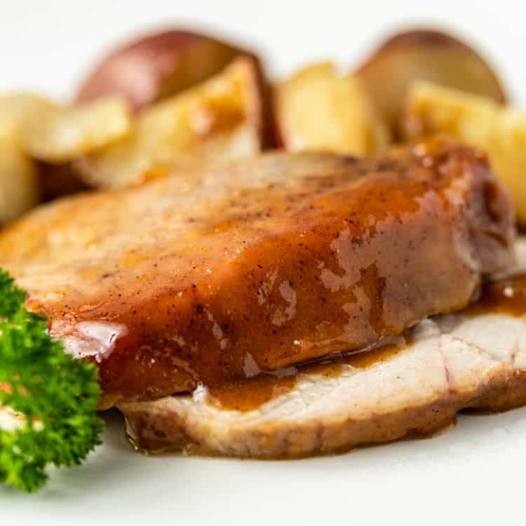 close up of sliced pork roast with apricot glaze and red potatoes in the background