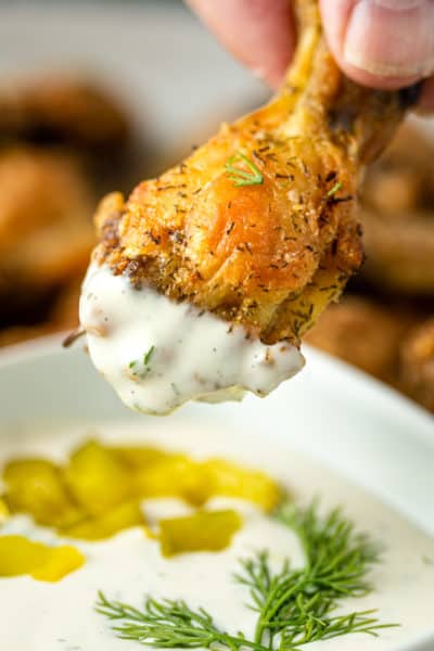 baked crispy chicken drumette being dipped into dill dipping sauce