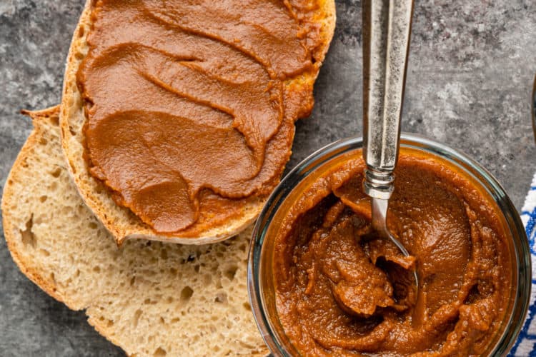 homemade pumpkin butter on slices of bread next to a full jar with a spoon