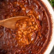 wooden spoon stirring pot of baked beans with bacon