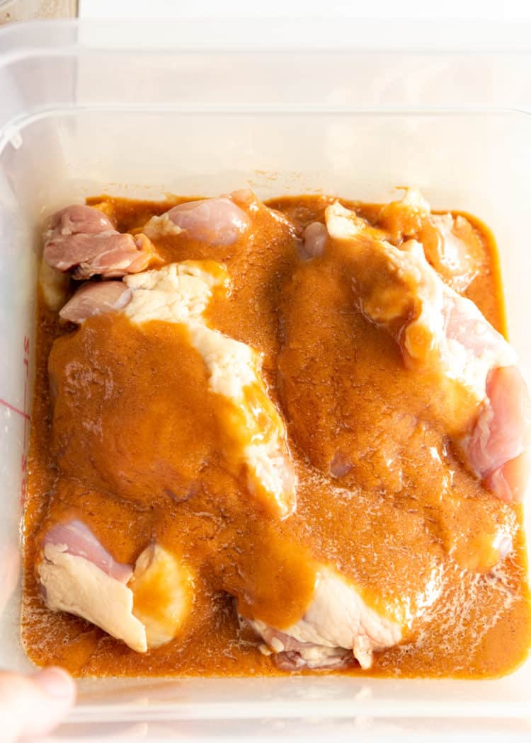 raw chicken marinating in clear plastic container