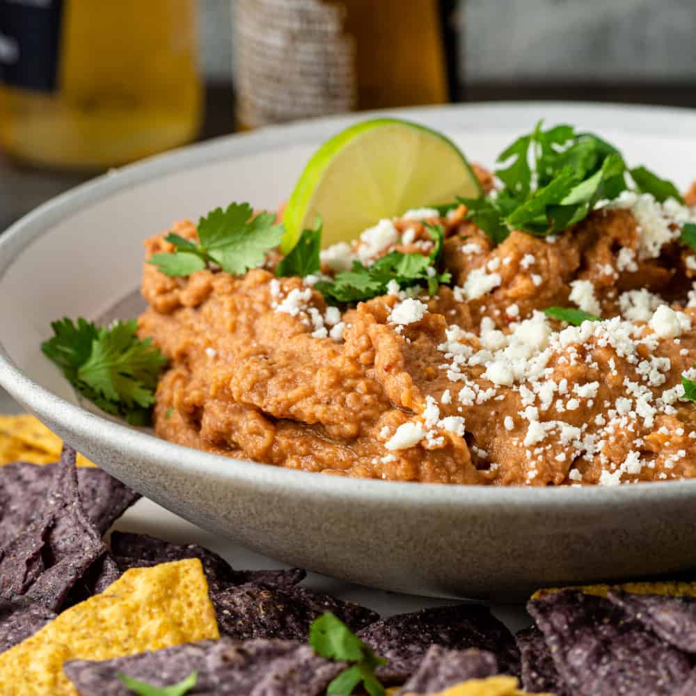 easy refried bean dip garnished with crumbled Mexican cheese in white bowl
