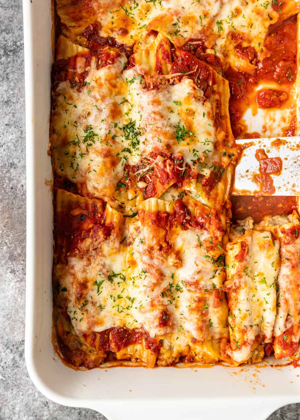 overhead of baked manicotti with tomatoe sauce in white pan