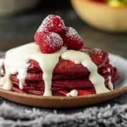 extreme closeup of short stack of fluffy red pancakes topped with white sugar syrup and fresh berries