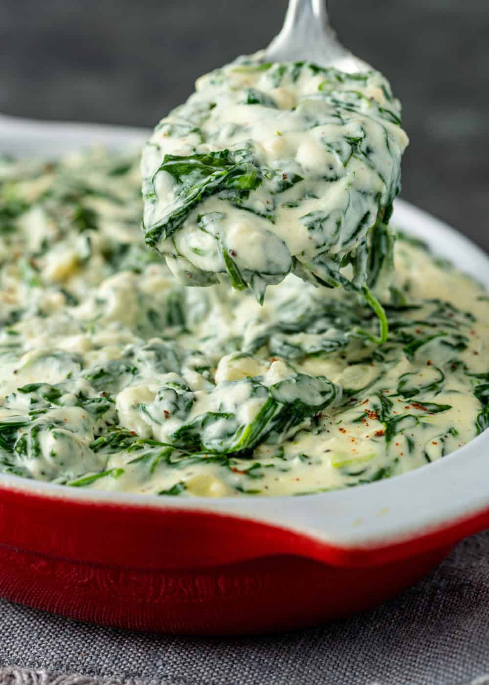 close up: spoonful of creamy spinach side dish above a serving dish of it