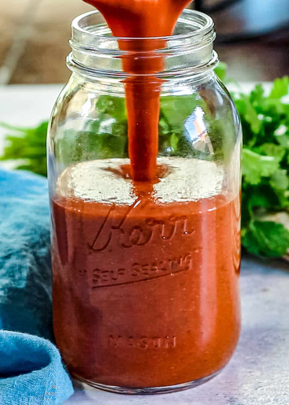 Mexican red sauce being poured into a glass mason jar