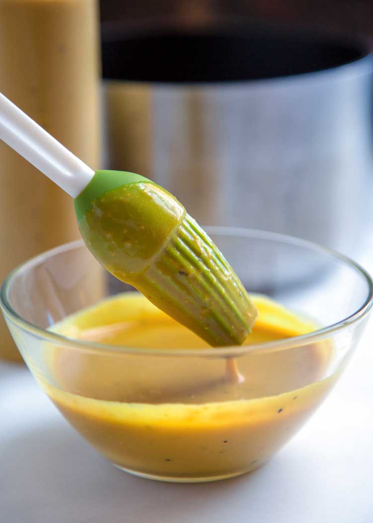 dipping green silicone basting brush into small glass bowl of mustard bbq sauce