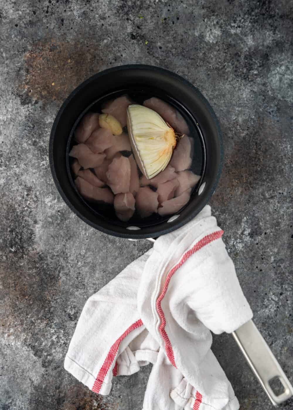 overhead image: half of a yellow onion and chunks of boneless pork cooking in small saucepan