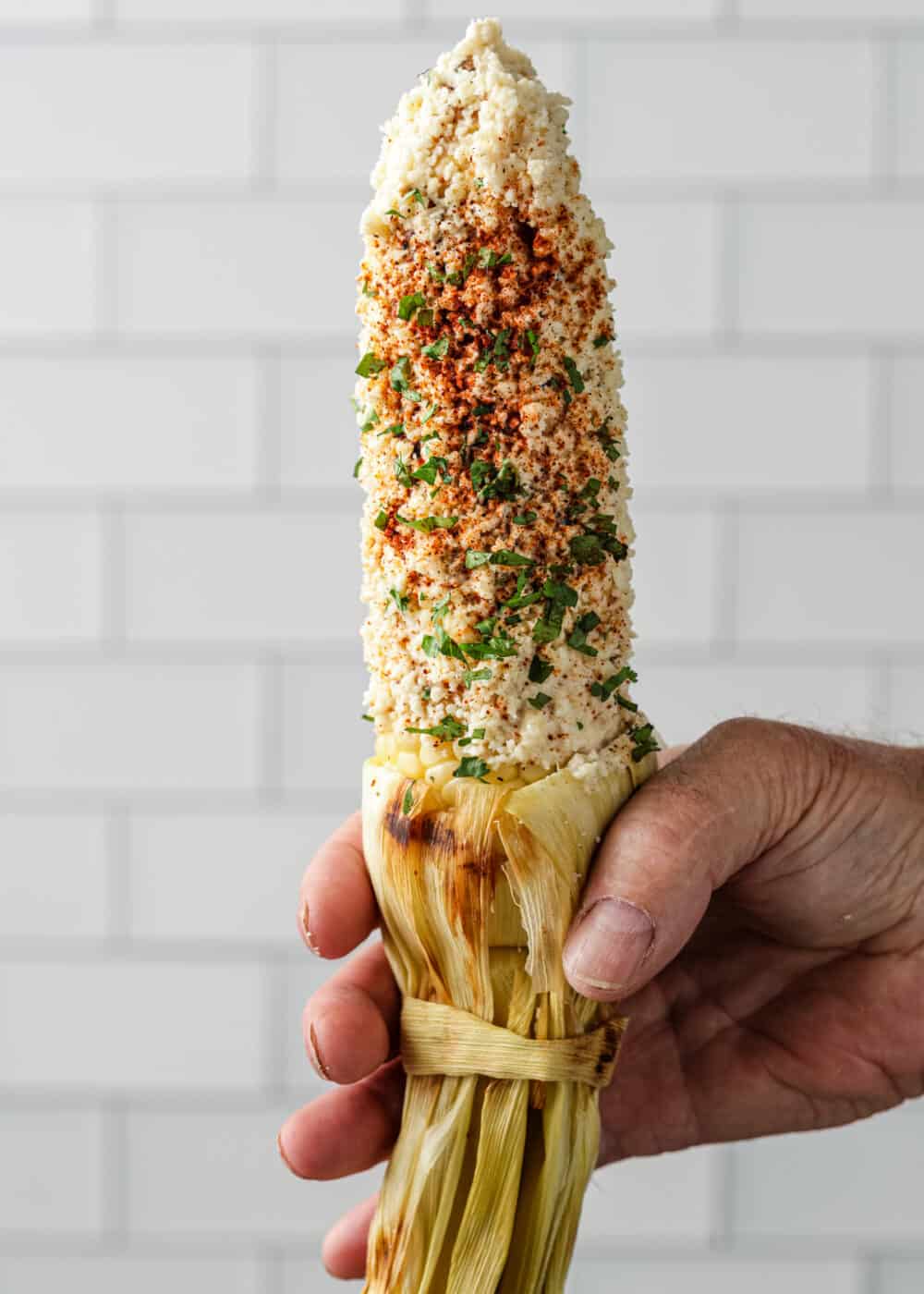 man's hand holding ear of Mexican corn on the cob