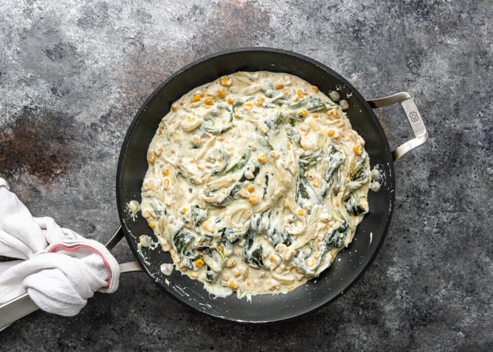 overhead image: large skillet filled with roasted poblanos in creamy white cheese sauce