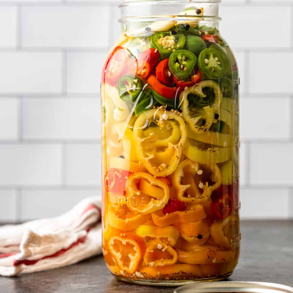 large mason jar with red yellow orange and green pickled peppers