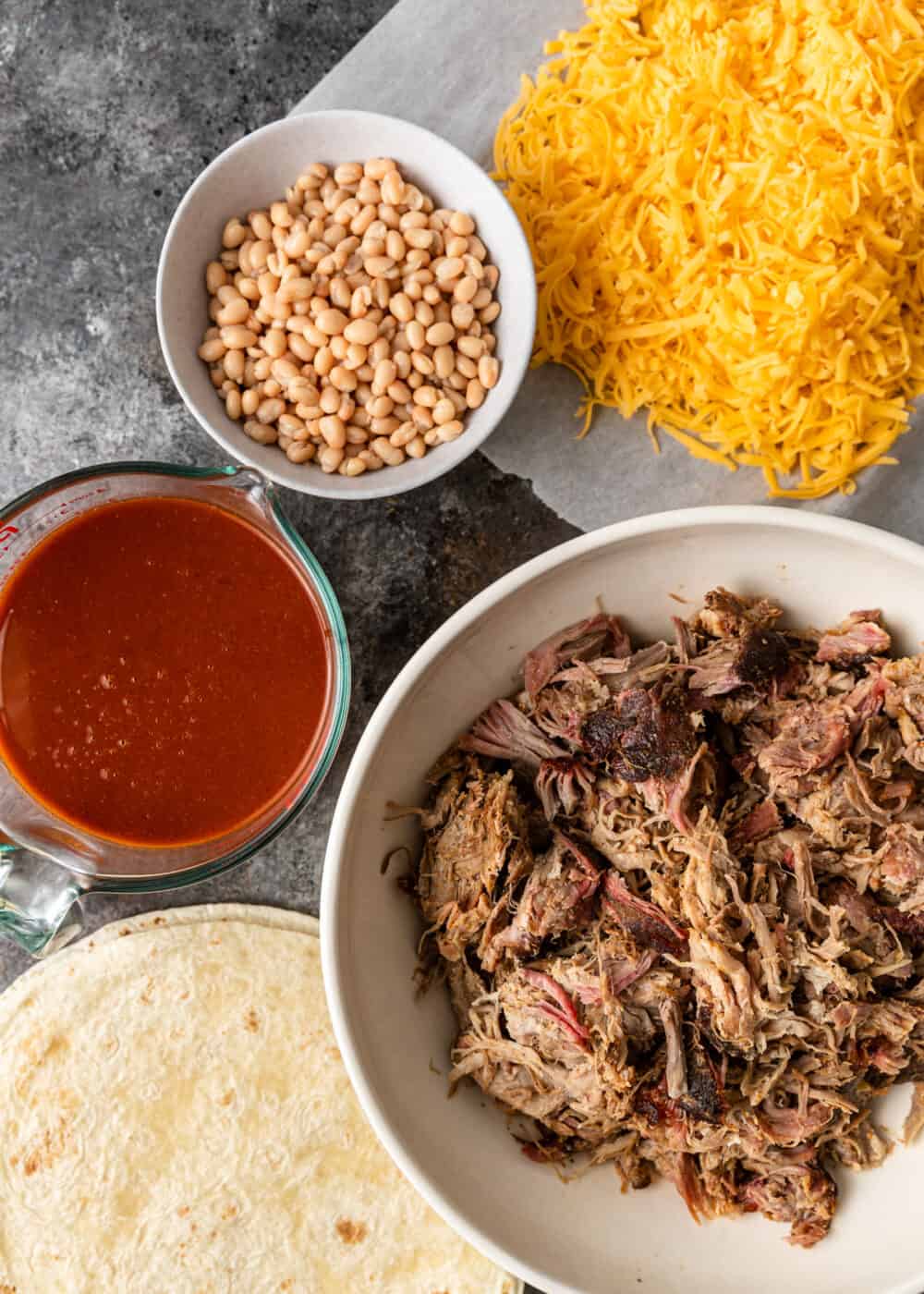 overhead: bowls of smoked pork, shredded cheese, white beans and red enchilada sauce
