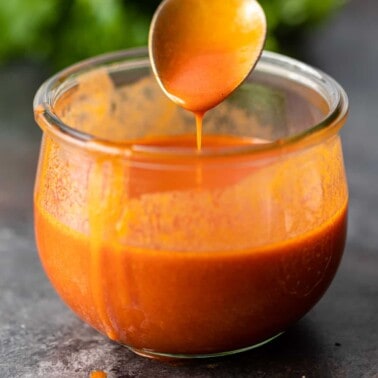 closeup: spicy wing sauce dripping off spoon into glass jar