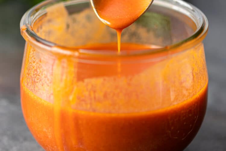 closeup: spicy wing sauce dripping off spoon into glass jar
