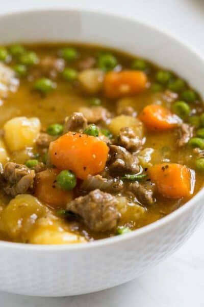 bowl of swiss steak stew made of tender beef in gravy with carrots, peas and potatoes
