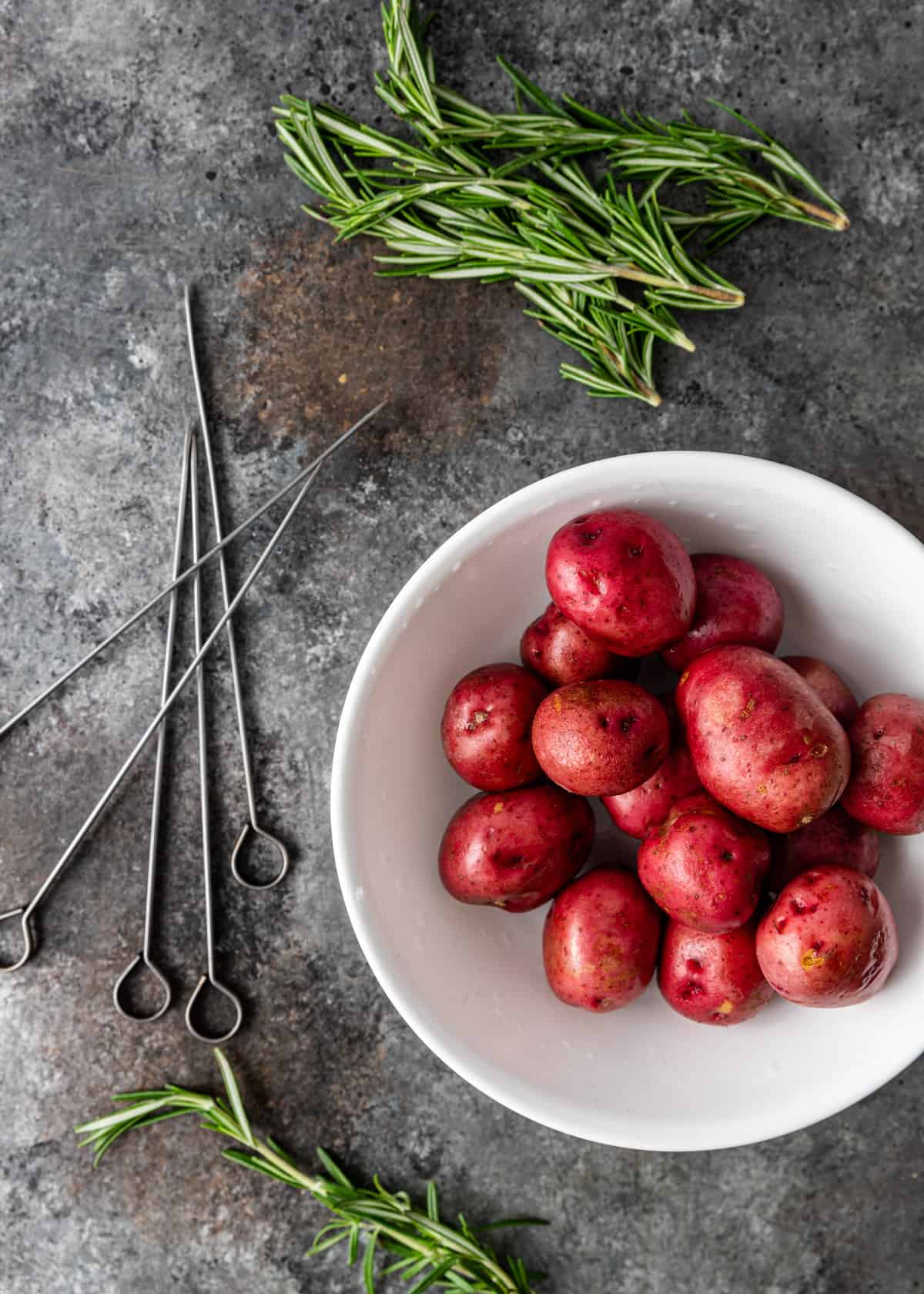 overhead: a bowl of red potatoes, metal skewers, and fresh rosemary