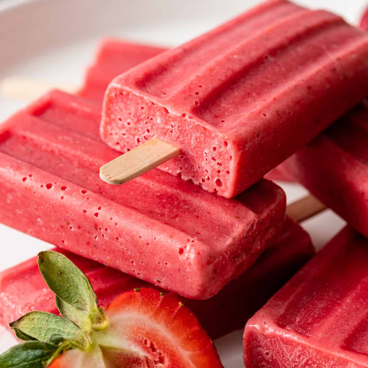closeup of strawberries and cream ice pops on a white plate with fresh strawberries