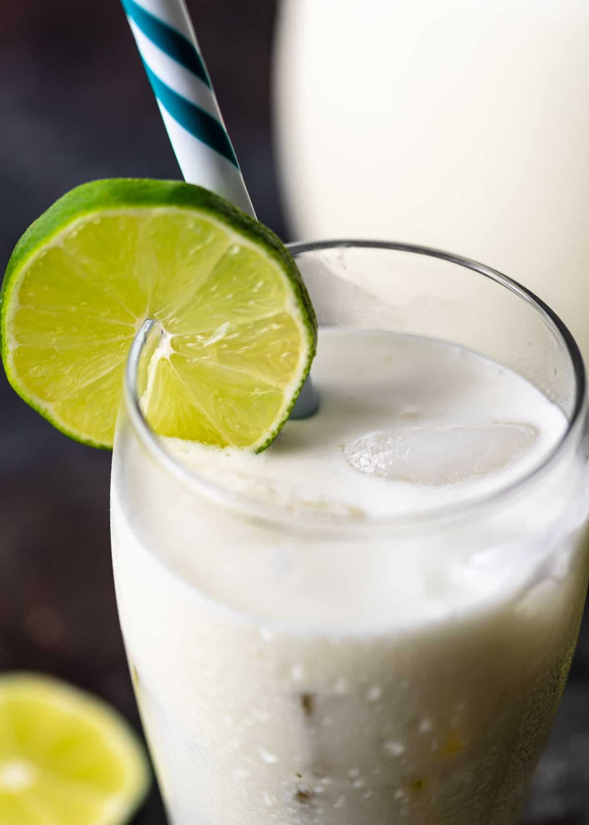 closeup: a cold glass of Brazilian lemonade with a lime round and a blue and white straw