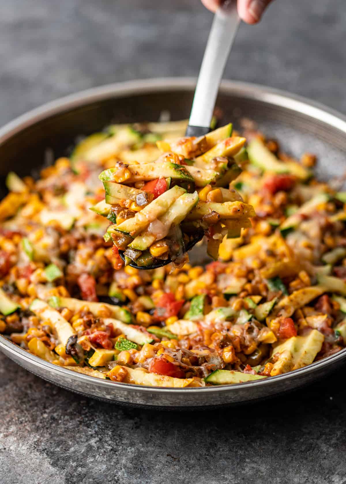 lifting calabacitas in a spoon over a large skillet with more Mexican zucchini