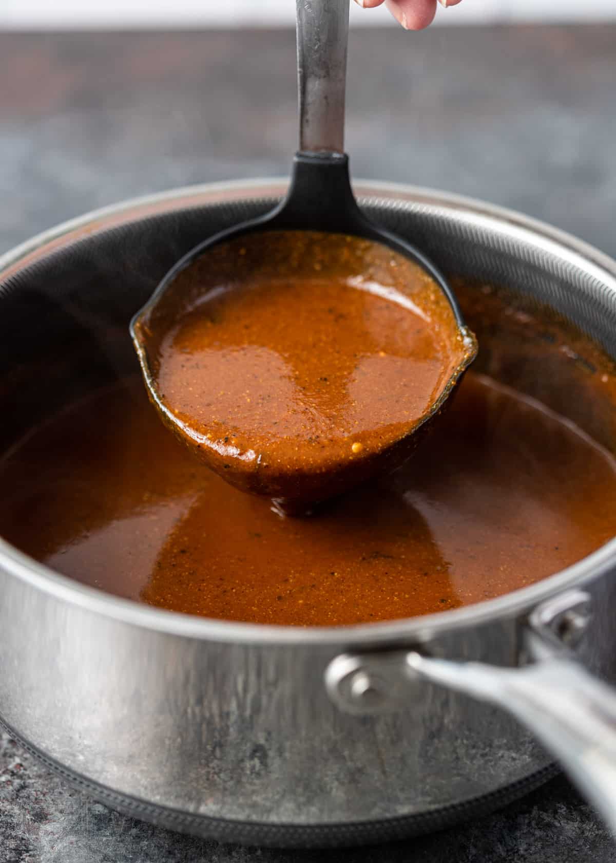 closeup: a ladle full of chili gravy over a pot with more gravy